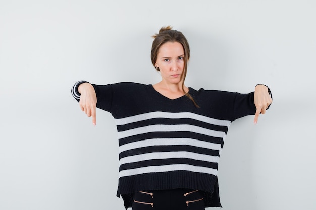 Free photo young lady pointing down in casual shirt and looking pensive