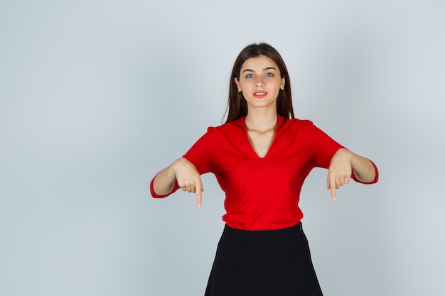 Young lady pointing down in red blouse, skirt and looking pretty