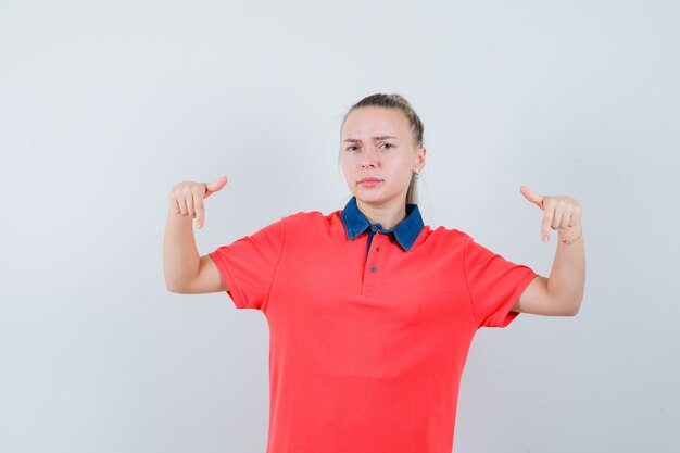 Foto gratuita giovane donna che punta verso il basso in maglietta e sembra seria