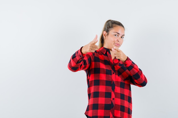 Foto gratuita giovane signora che indica davanti in camicia controllata e che sembra sicura