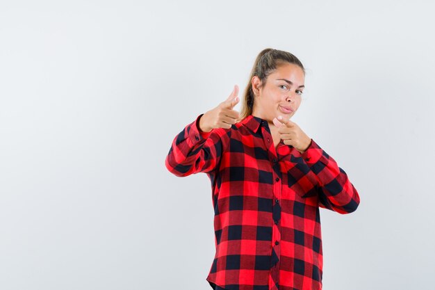 Young lady pointing at front in checked shirt and looking confident