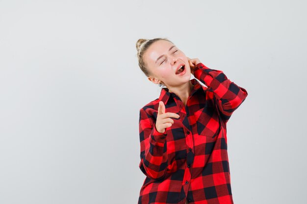 Young lady pointing at front in checked shirt and looking delighted