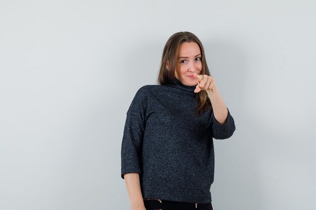 Young lady pointing at front in shirt and looking optimistic