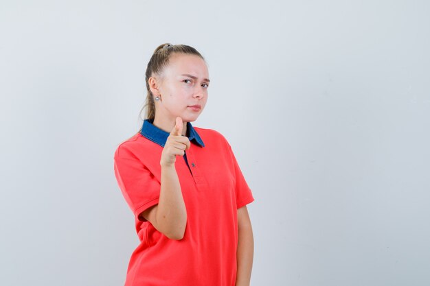 Young lady pointing at front in t-shirt and looking suspicious