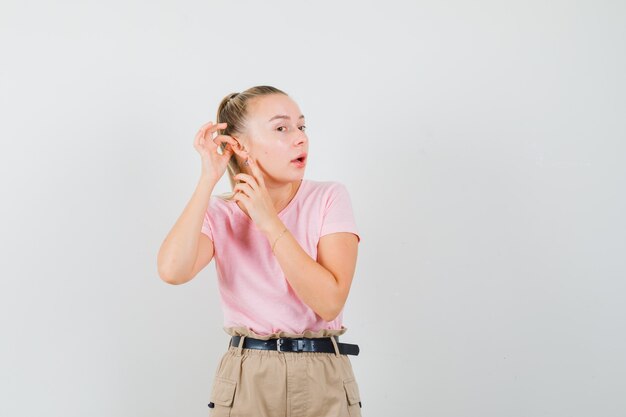 Young lady pointing at her ear in t-shirt and pants