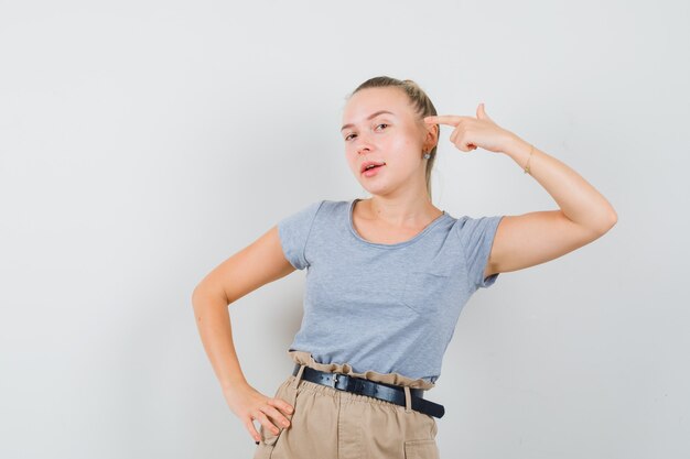 Tシャツとズボンで頭を指して自信を持って見える若い女性