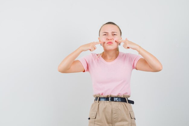 Young lady pointing at her upper lip in t-shirt and pants