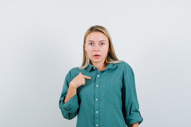 Young lady pointing at herself in green shirt and looking puzzled.