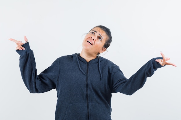 Young lady pointing at left and right at the same time in jacket and looking hesitant. front view.