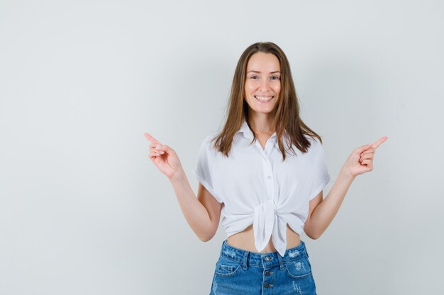 Young lady pointing to left and right sides in white blouse and looking happy. front view.