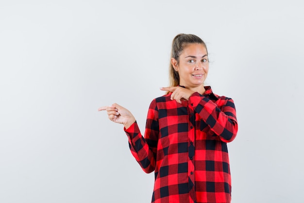 Young lady pointing to the left side in checked shirt and looking merry