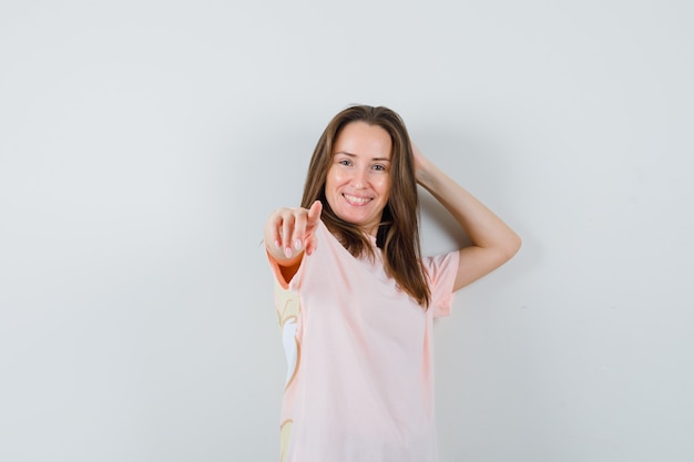 Young lady pointing in pink t-shirt and looking merry. front view.