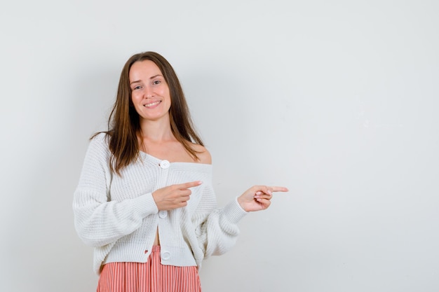 Young lady pointing to the right side in cardigan and skirt looking pretty isolated