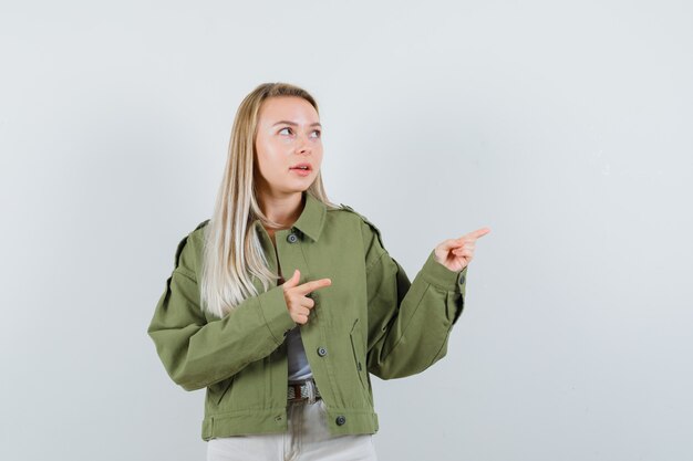 ジャケット、パンツ、物思いにふける、正面図で右側を指している若い女性。