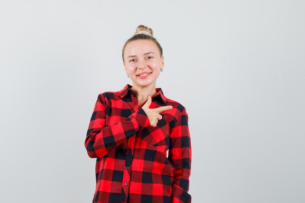 Young lady pointing to the side in checked shirt and looking cheerful