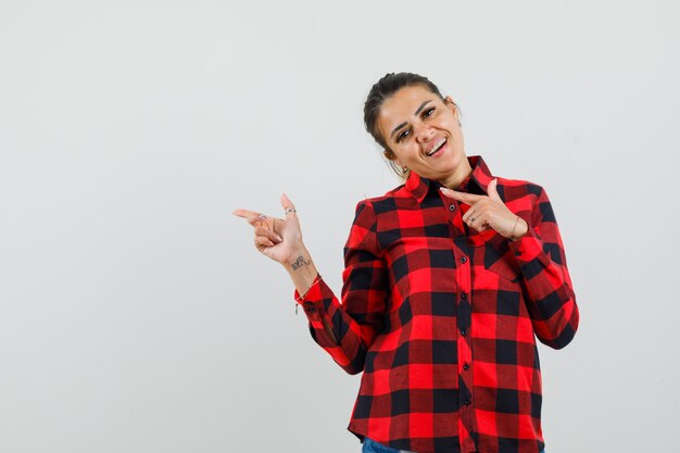 Young lady pointing to the side in checked shirt and looking cheery