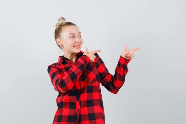 Free photo young lady pointing to the side in checked shirt and looking cheery