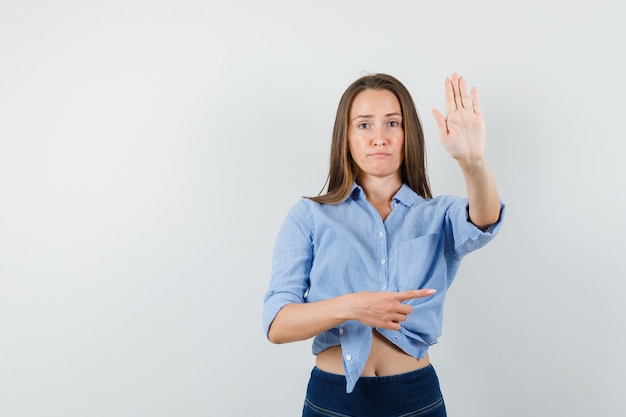 Young lady pointing to side and showing stop gesture in blue shirt