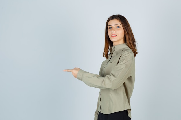 Young lady pointing straight ahead in shirt, skirt and looking cheerful .