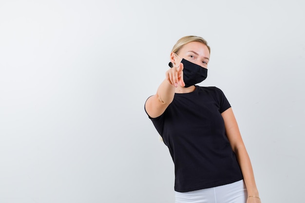 Young lady pointing in t-shirt, pants, medical mask and looking confident