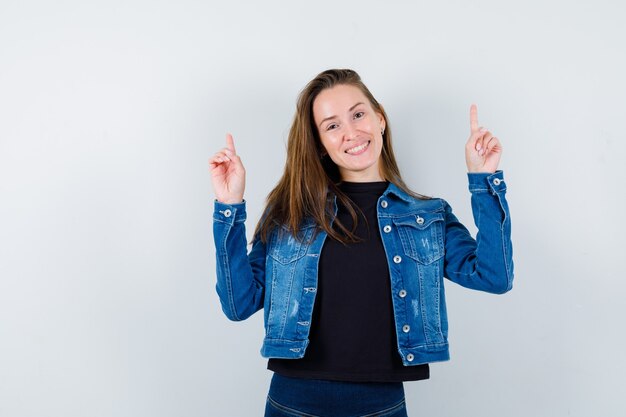 Young lady pointing up in blouse, jacket and looking cheery. front view.