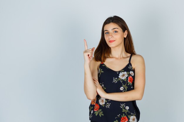 Young lady pointing up in blouse and looking hopeful. front view.