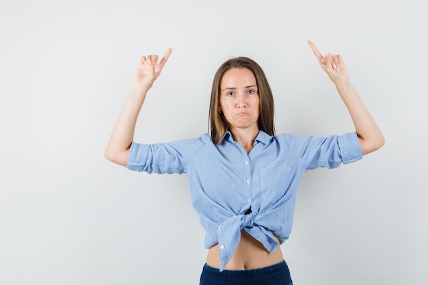 Free photo young lady pointing up in blue shirt, pants and looking disappointed