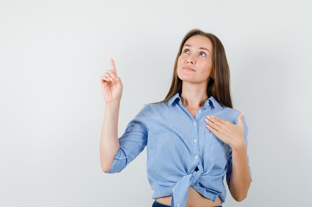 Young lady pointing up in blue shirt, pants and looking hopeful