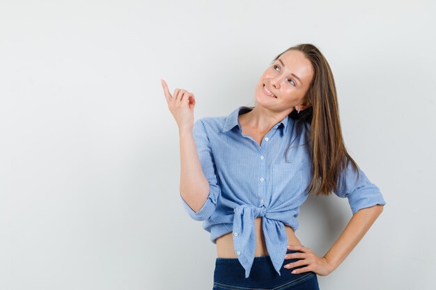 Young lady pointing up in blue shirt, pants and looking merry