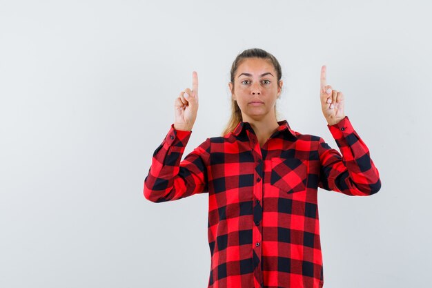 Young lady pointing up in casual shirt and looking confident. front view.