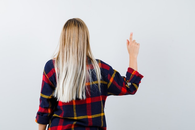 Young lady pointing up in checked shirt and looking confident , back view.