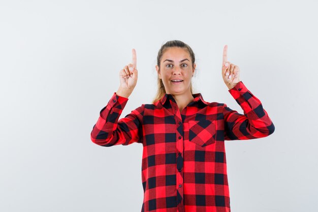 Young lady pointing up in checked shirt and looking confident