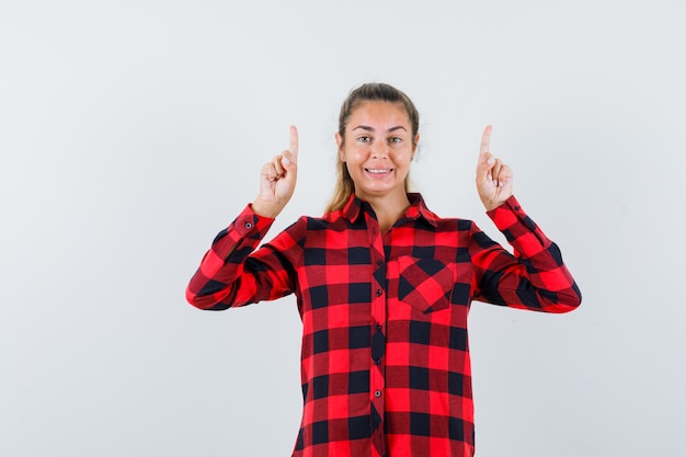 Young lady pointing up in checked shirt and looking happy