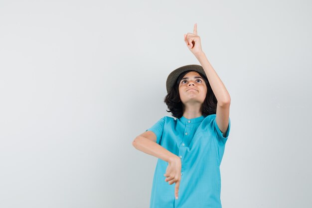 Young lady pointing up and down in blue shirt, hat and looking concentrated.