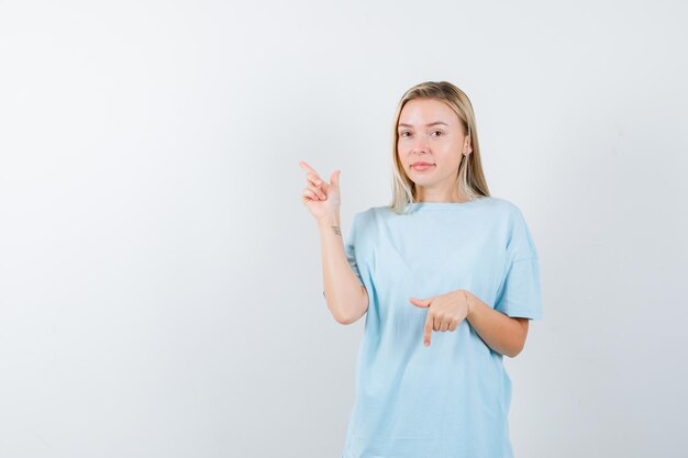 Young lady pointing up and down in t-shirt and looking hesitant isolated