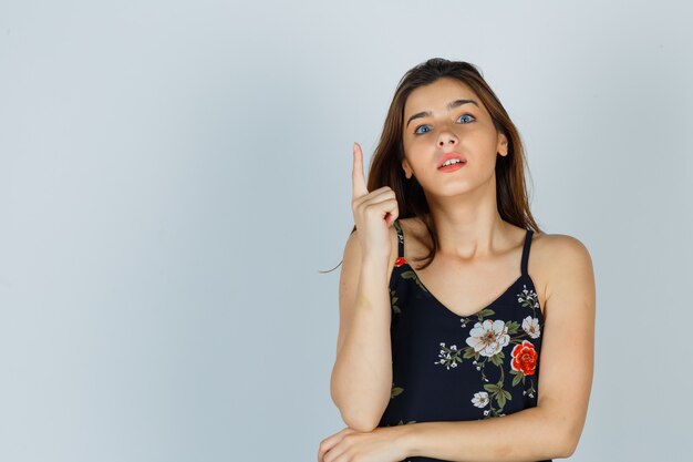 Young lady pointing up in floral top and looking shocked