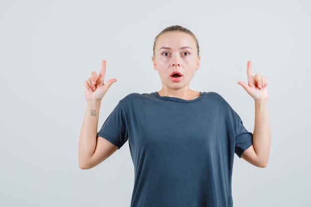 Young lady pointing up in grey t-shirt and looking puzzled