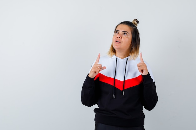 Free photo young lady pointing up in hoodie sweater and looking pensive