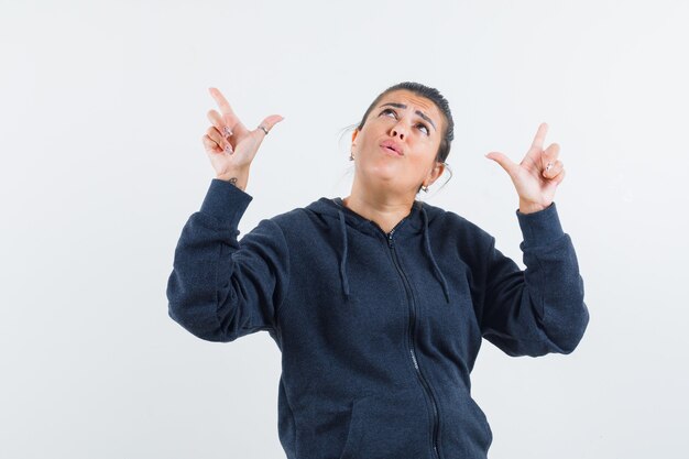 Young lady pointing up in jacket and looking astonished 