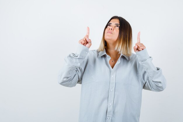 Young lady pointing up in oversized shirt and looking thoughtful. front view.