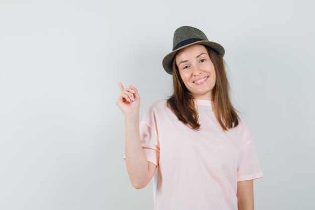 분홍색 티셔츠 모자를 가리키는 쾌활한 찾고 젊은 아가씨