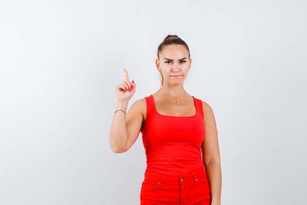 Young lady pointing up in red singlet, red trousers and looking confident , front view.