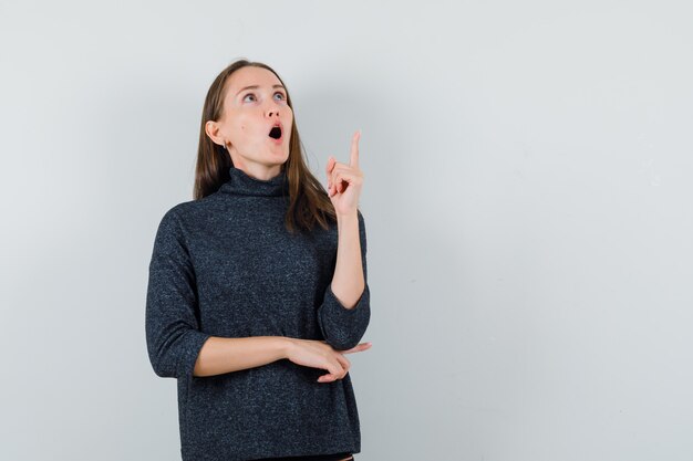 Young lady pointing up in shirt and looking amazed