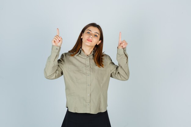 Young lady pointing up in shirt, skirt and looking confident