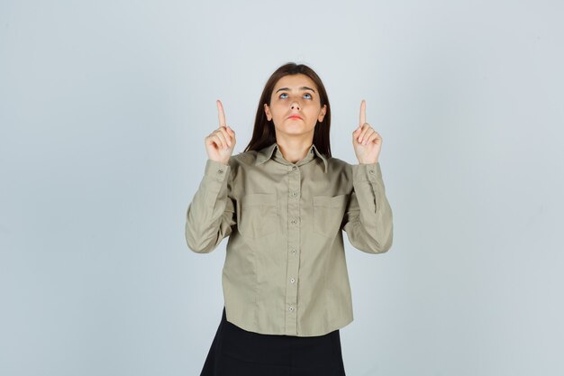 Young lady pointing up in shirt, skirt and looking disappointed