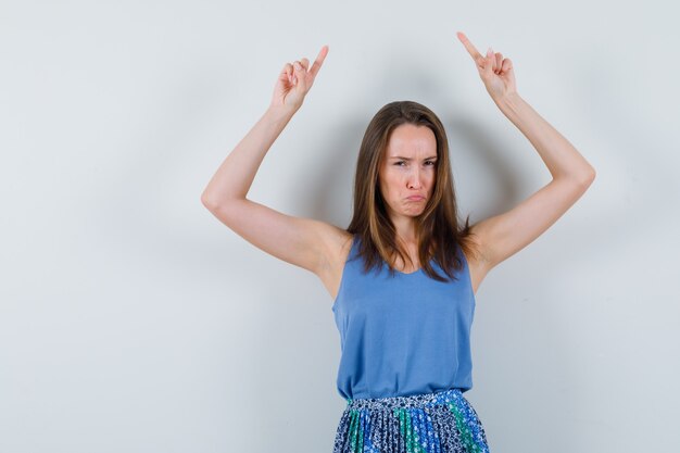 Young lady pointing up in singlet, skirt and looking gloomy