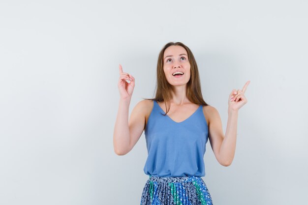 Young lady pointing up in singlet, skirt and looking hopeful. front view.