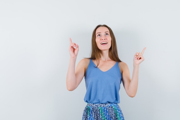 Young lady pointing up in singlet, skirt and looking hopeful. front view.