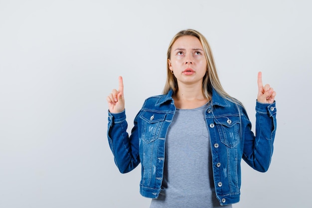 Young lady pointing up in t-shirt, denim jacket, skirt and looking thoughtful.