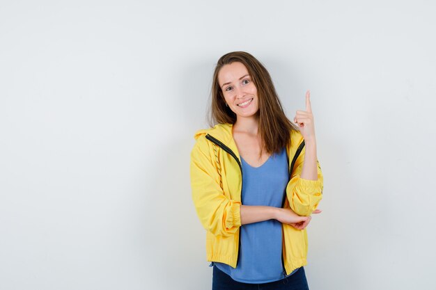 Young lady pointing up in t-shirt, jacket and looking confident. front view.